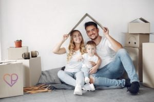 young family moving into new house they have purchased. They are holding a cardboard box over their head to illustrate life insurance and critical illness cover. the young handsome couple have a young child