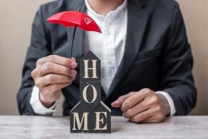 man holding a red umbrella over blocks that spell out "home". This represents mortgage life insurance and critical illness cover. The man is well dressed in a nice suit. 