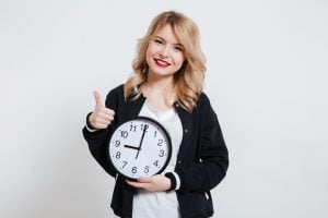 blonde haired woman holding a clock with her thumb up as she's just saved time setting up her life insurance by using a broker