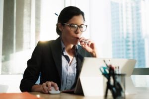 young business woman sittinga t a desk working on amicrosoft surface while smoking an e-cigarette